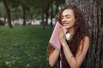 girl student holding book and sitting under tree