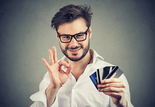 Smiling man showing OK gesture and credit cards