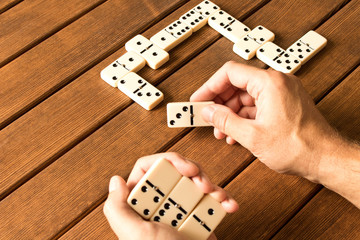 Playing dominoes on a wooden table. Man's hand with dominoes