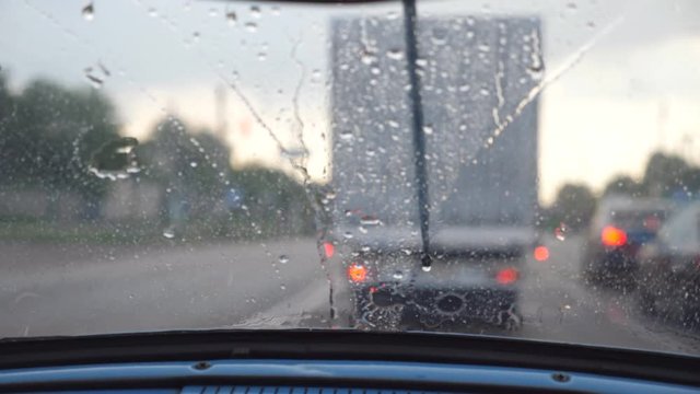 POV from the front seat to windshield of old retro car during bad weather. Wipers removing raindrops from the window of vintage automobile during ride on the highway. Close up Slow motion