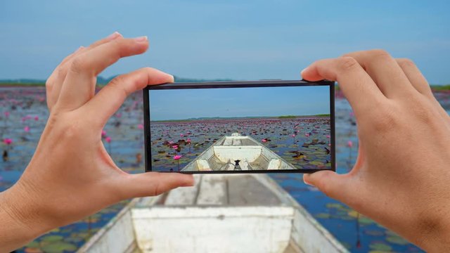 Cinemagraph of Taking Mobile Photo of Riding Wooden Longtail Boat among Red Lotus Flowers. Front View at Thale Noi Waterfowl Reserve Lake, Thailand