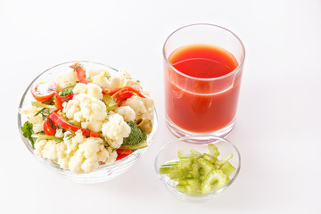 Fresh salad of cauliflower with tomato, broccoli, olives, sweet pepper, herbs, celery and a glass of tomato juice on white background