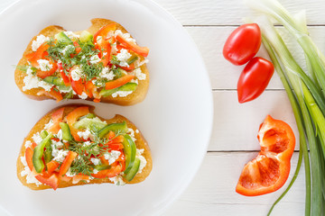 Two bruschettes with red sweet pepper and goat cheese in a plate on the background of fresh vegetables. Top view