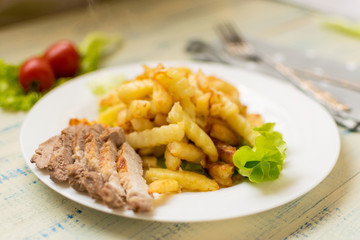 French fries with meat on a white plate on a wooden light background.