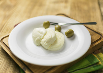 Cheese mozzarella and olives on a plate on a wooden background.