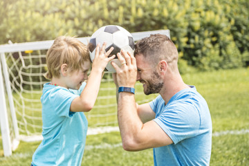 Fototapeta premium Man with child playing football outside on field