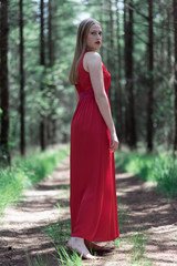 Obraz na płótnie Canvas Blonde woman in red dress on forest path looking over shoulder.