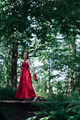 Obraz na płótnie Canvas Woman in red dress crossing wooden bridge in summer forest.
