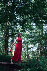 Naklejka premium Woman in red dress crossing wooden bridge in summer forest.