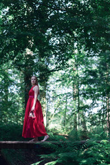 Woman in red dress crossing wooden bridge in summer forest.