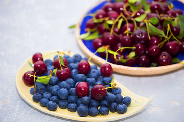 Delicious and fresh berries in summer. On the table are bowls of cherries and blueberries close-up