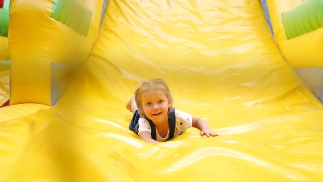 Happy childhood - little kid girl slides down the inflatable slide outdoor trampoline