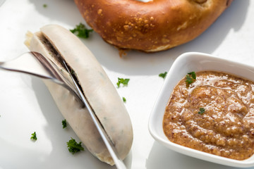 Frau isst Münchener Weißwurst mit Messer und Gabel, süßen Senf und Brezel und löst Wurst richtig aus Pelle