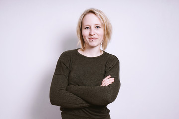 portrait of a blue-eyed blonde confident young woman with arms crossed standing in front of...