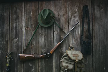 Foto auf Acrylglas Jagd Professionelle Jagdausrüstung für die Jagd. Gewehr, Hut, Tasche und andere auf schwarzem Holzhintergrund.
