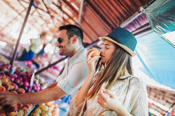 Young couple buying fruits and vegetables in a market on a sunny morning.
