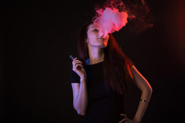 Young woman in neon light and smoke of e-cigarettes or vape on black background
