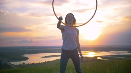 Cheerful young woman rotates hoop on the hand at sunset on the hill