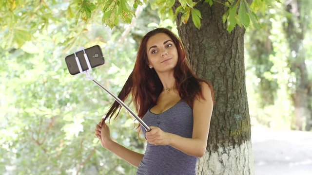 Taking selfie stick photo of cute busty girl posing with smart phone for social media