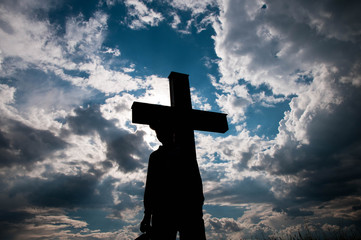 Silhouette of a young boy and a catholic cross at sundown, dramatic storm clouds background.