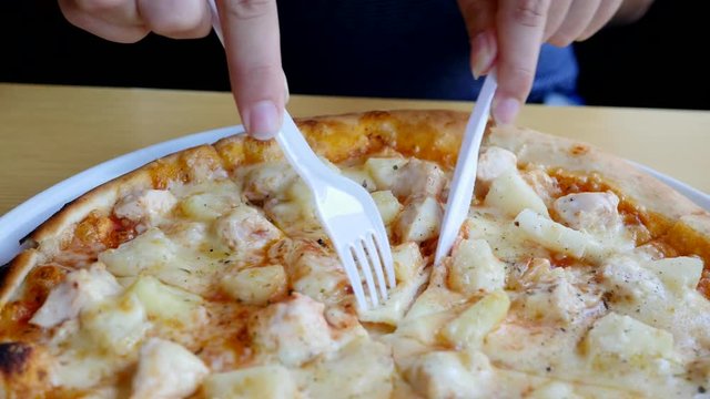 Cutting slicing a piece of pizza circle on plate in fast food restaurant with plastic fork and knife