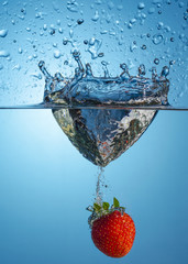 one strawberry berry falling into the water on a blue background