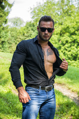 Handsome Hunk Man Outdoor in City Park, Opening his Shirt to Show Muscular Torso and Chest During...