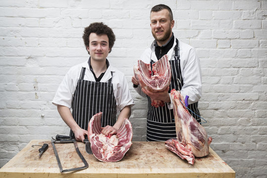 Two butchers side by side holding meat joints, part of a large butchered carcass.