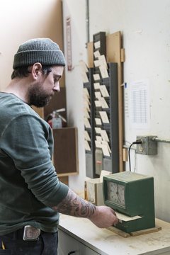 A Caucasian carpenter checking in with a time clock in a woodworking factory.