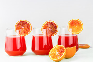 three glass of red orange juice and oranges, isolated on white background