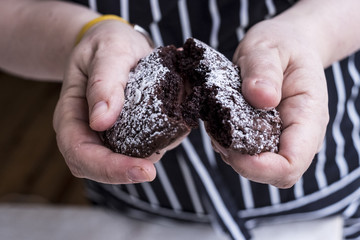 A cook in an apron holding a dark chocolate brownie cake broken in half