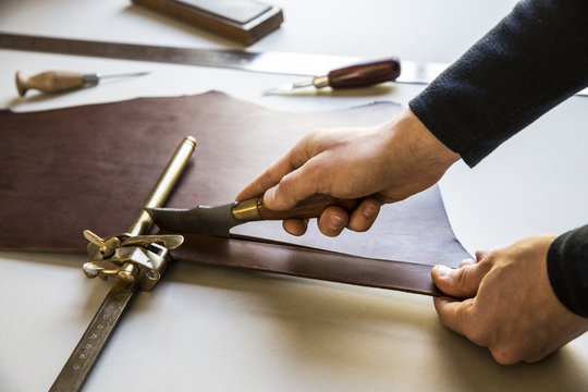 High angle close up of craftsman making brown leather camera strap, clamping the leather pieces together, and using hands tools. 