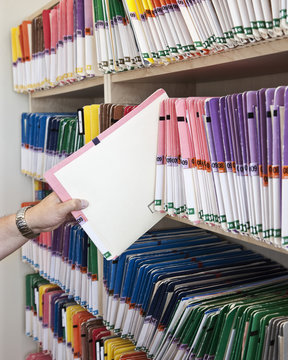 A closeup of a hand removing a file folder from a group of file folders on shelves in an office.