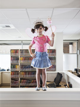 A young Caucasian girl dressed up as a fairy standing on a reception desk in a dental practice.