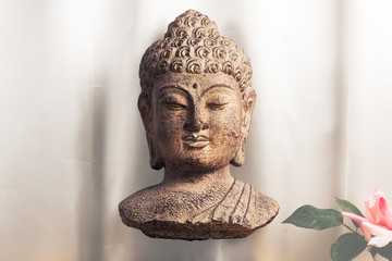 Bust of the Buddha with a cracked paint finish floating in front of a silk background. Some leaves and a rose can be partially seen in the bottom right corner.