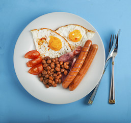 Plate of breakfast with fried eggs, bacon beans tomatoe slices isolated on blue background Square Image
