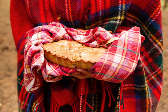 Woman In Red Scottish Plaid Is Holding Apple Pie On Red Checkered Towel In Autumn Forest.