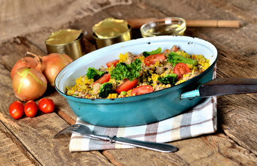 Tuna risotto with vegetables, tomatoes, broccoli and parsley in the old pan, onions, cans and oil in the background