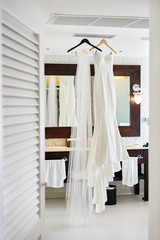 Fototapeta na wymiar Mermaid wedding dress and long veil hanging in the white room, reflection in the mirror