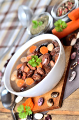Bean soup with large beans on cutting board, carrots, parsley, marjoram, spoon and ladle - vertical photo
