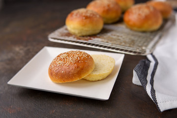 Homemade Hamburger Buns Topped with Sesame Seeds on a Rustic Black Background; One Cut Open on White Square Paper Plate