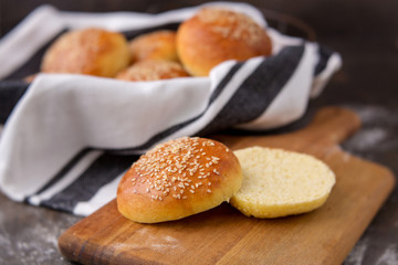 Homemade Hamburger Buns Topped with Sesame Seeds in Wire Bread Basket; One Cut open on Wood Cutting Board