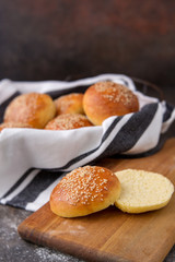 Homemade Hamburger Buns Topped with Sesame Seeds in Wire Bread Basket; One Cut open on Wood Cutting Board