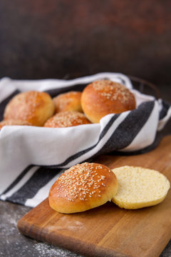Homemade Hamburger Buns Topped with Sesame Seeds in Wire Bread Basket; One Cut open on Wood Cutting Board