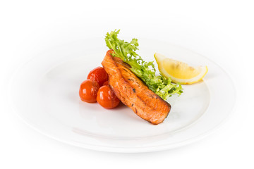 fried salmon fish with fresh salad, tomatoes and lemon on white plate