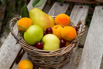fruit basket is on the bench, it is composed of pear, apples, cherries and apricots
