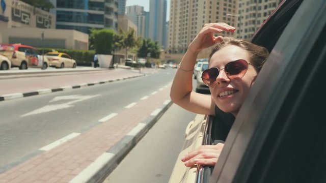 A happy girl sits on the back seat of a car and travels around the city of Dubai.