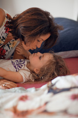 beautiful mother cuddles with her daughter in bed, giggling and laughing and kissing, beautiful...