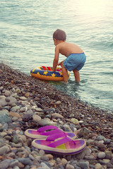 A little boy is swimming with an inflatable circle on the seashore