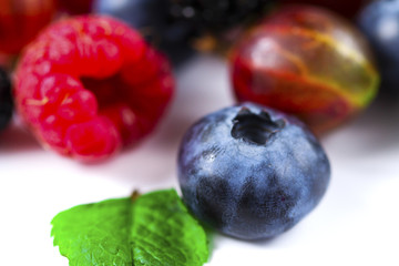 Close-up arrangement mixed, assorted berries including blackberries, strawberry, blueberry, raspberries and fresh leaf on white